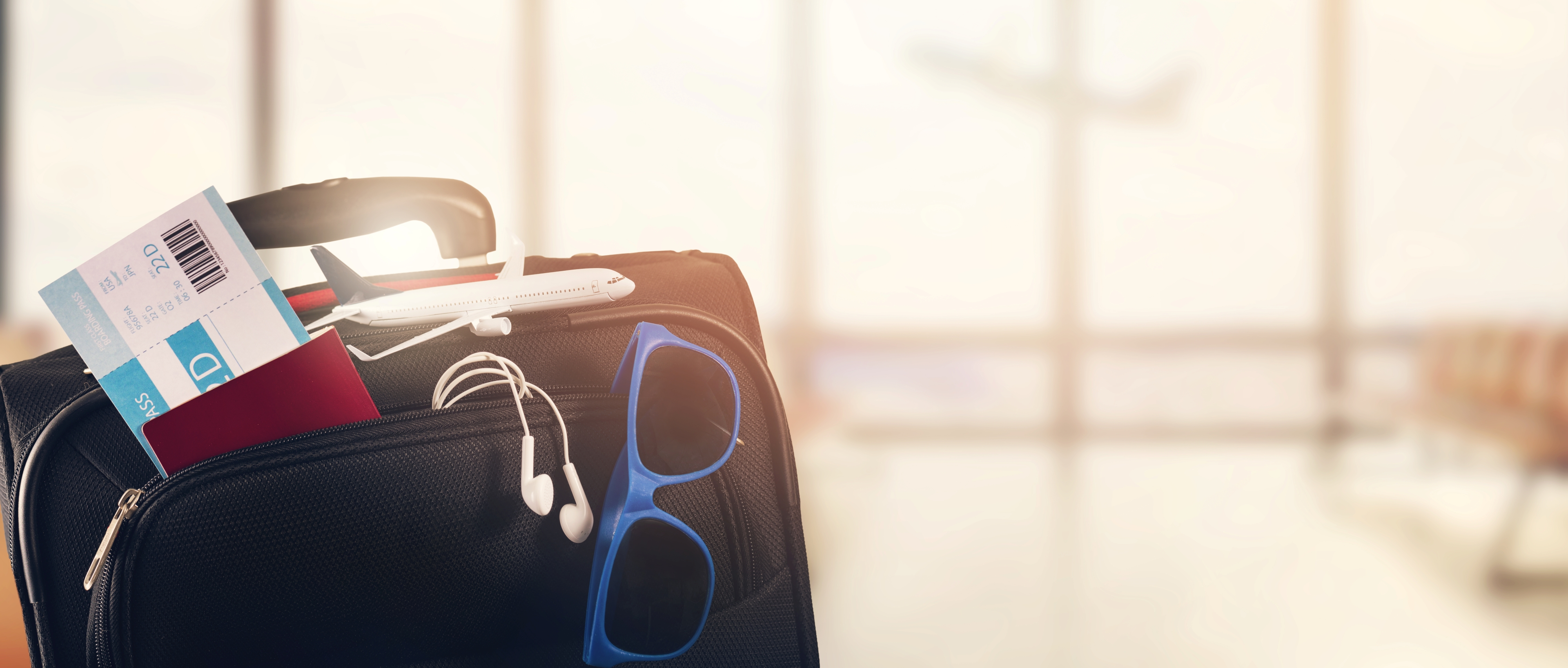 Open luggage bag with earbuds, plane ticket and sunglasses.